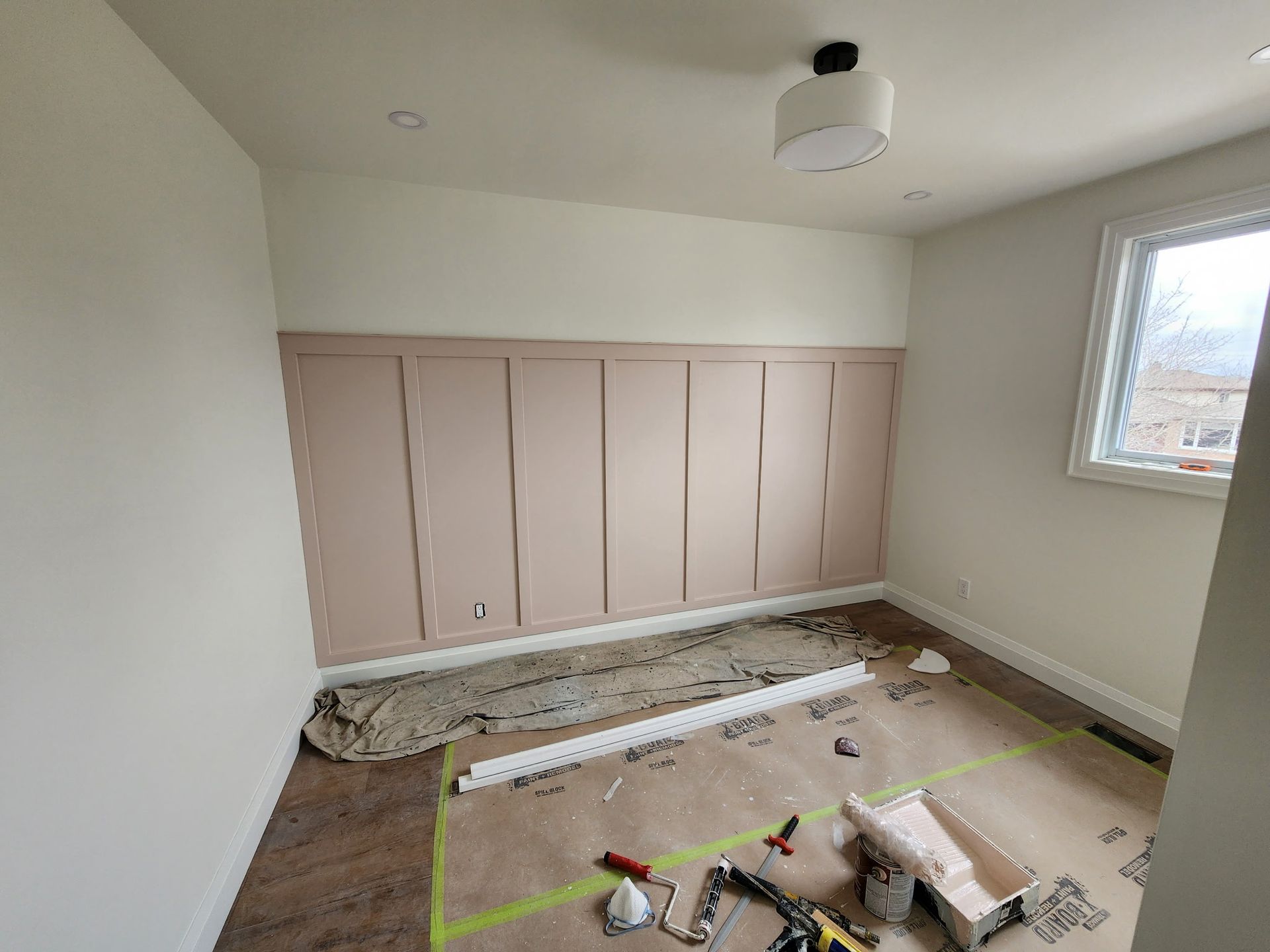 Room with wall paneling and a window, under construction. The walls are white and pink.