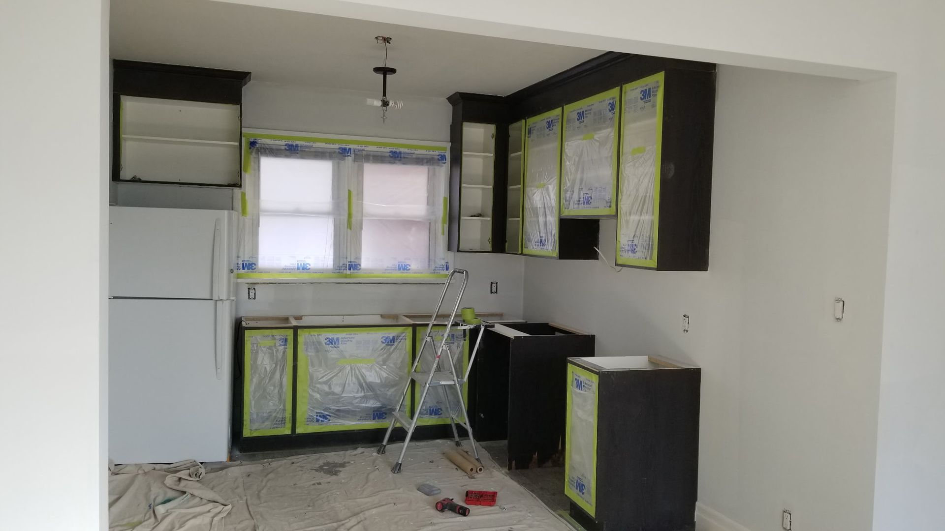 Kitchen under renovation with dark cabinets, covered in protective plastic, and white walls.