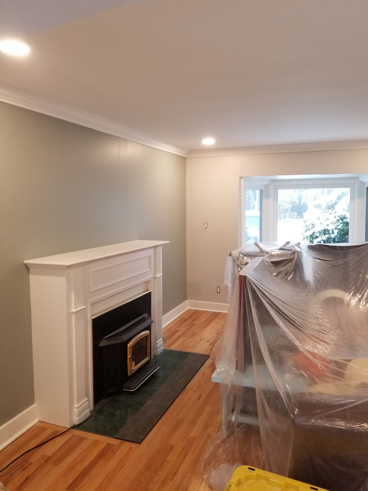 Living room with fireplace, painted walls, crown molding, hardwood floors, and bay window.
