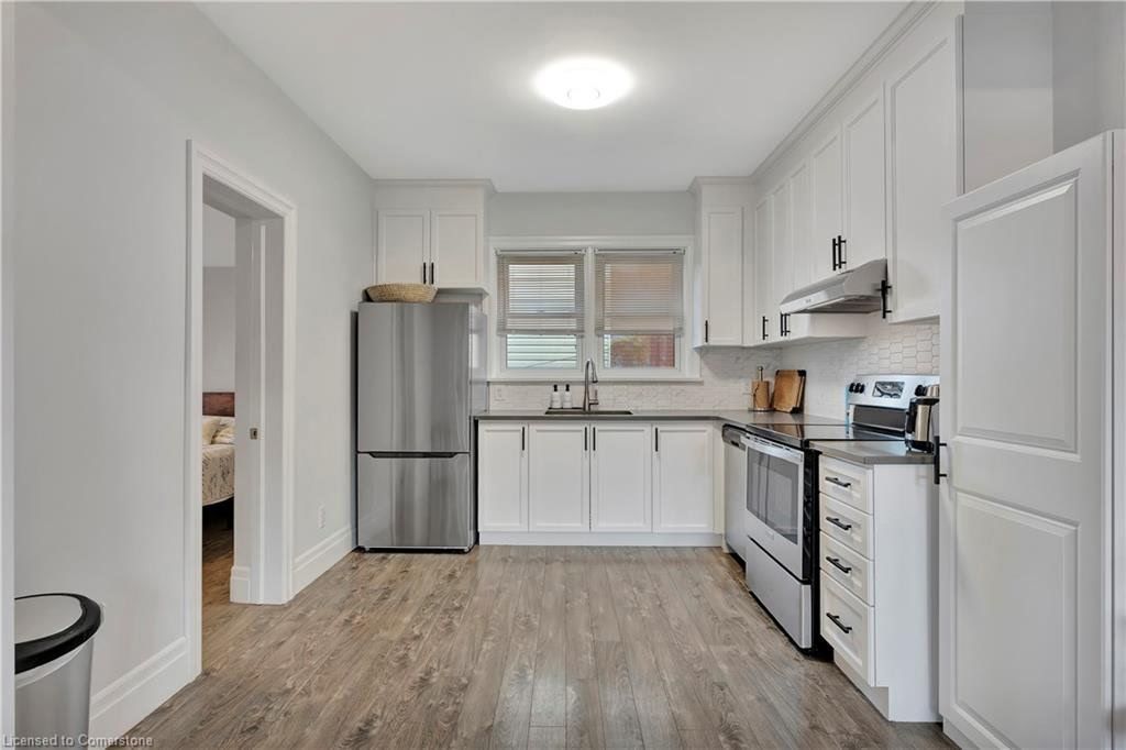 White kitchen with stainless steel appliances, white cabinets, and gray flooring.