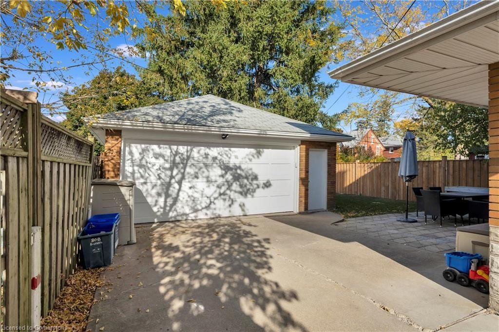 Concrete driveway leading to a detached garage. A fence is on the left, and a patio with furniture on the right.