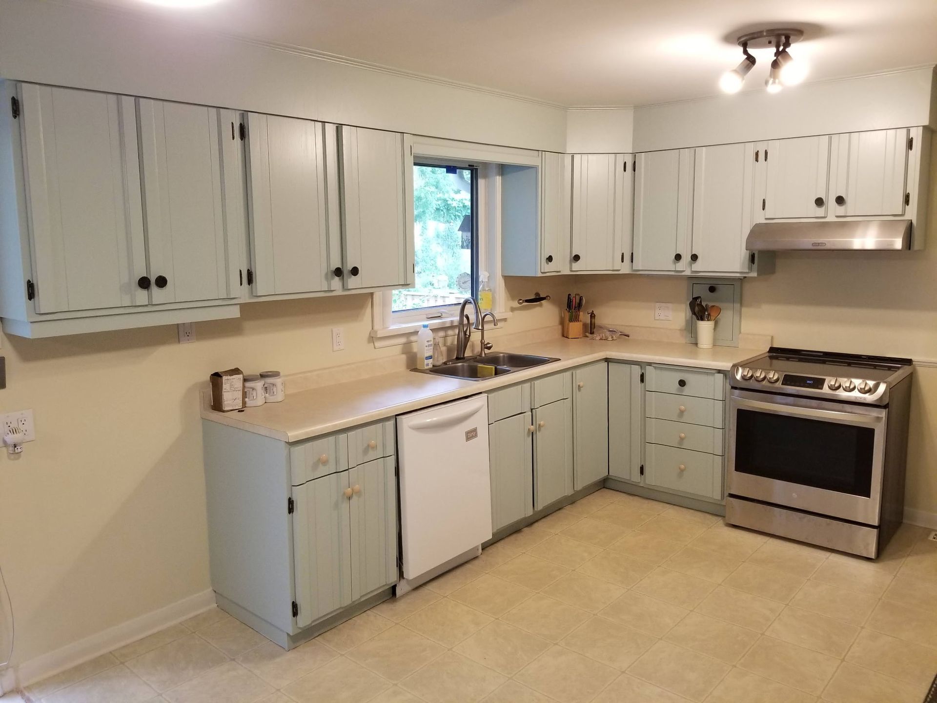 A kitchen with light blue cabinets, stainless steel appliances, and a window.