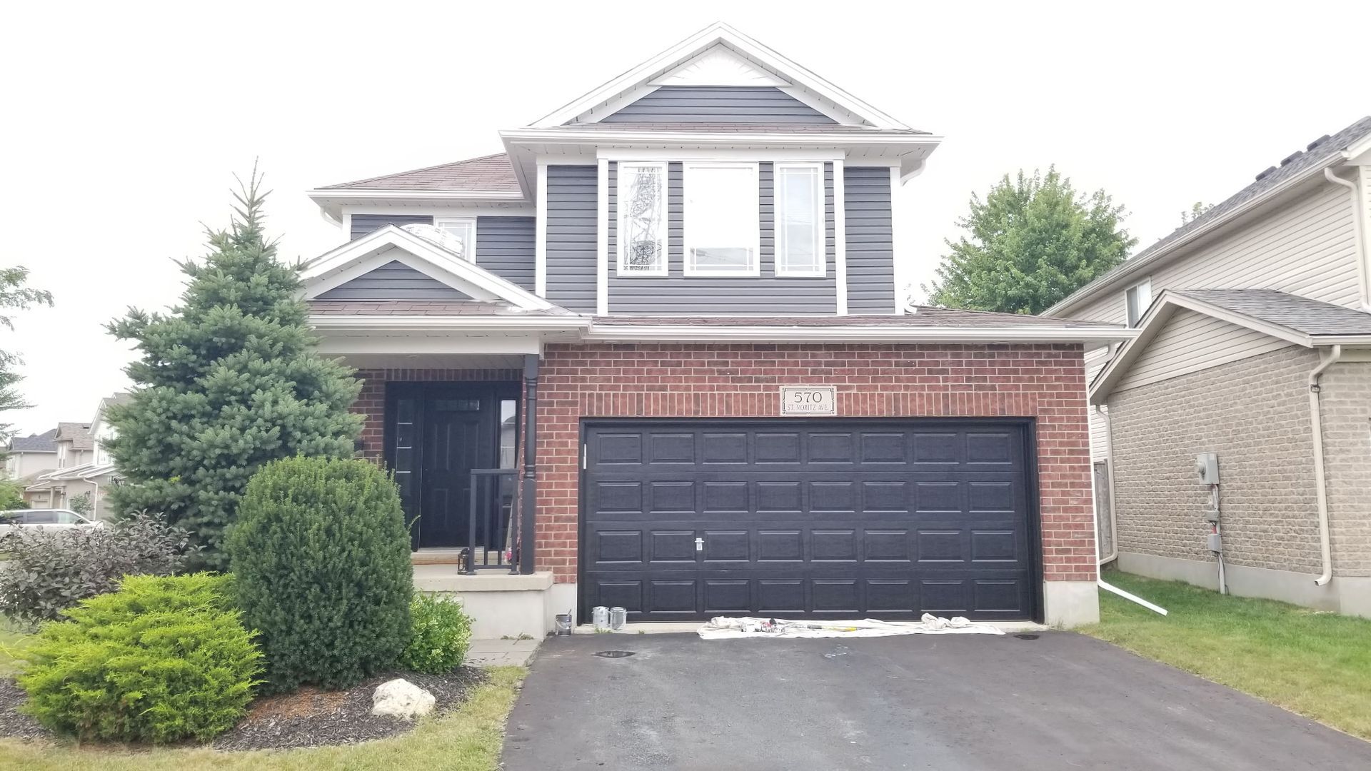 Two-story house with brick and gray siding, black garage door, and a paved driveway.