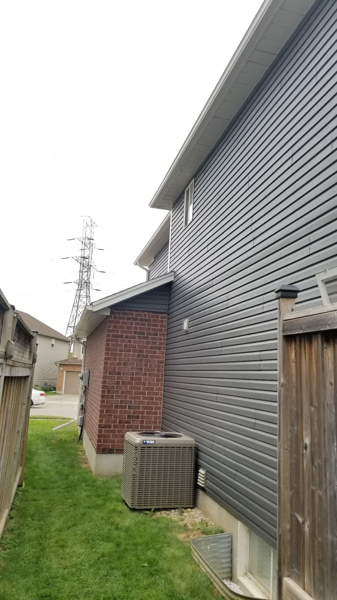 Exterior of a two-story house with dark gray siding. A brick structure and air conditioning unit are visible at the base of the wall.