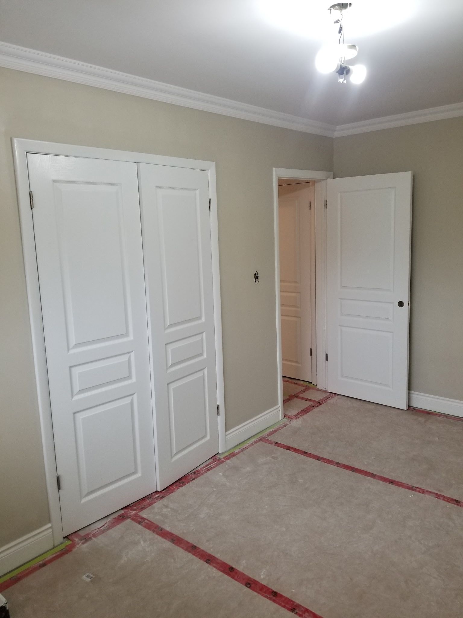 Empty room with white doors, tan walls, and light fixture on ceiling. Red lines on floor.