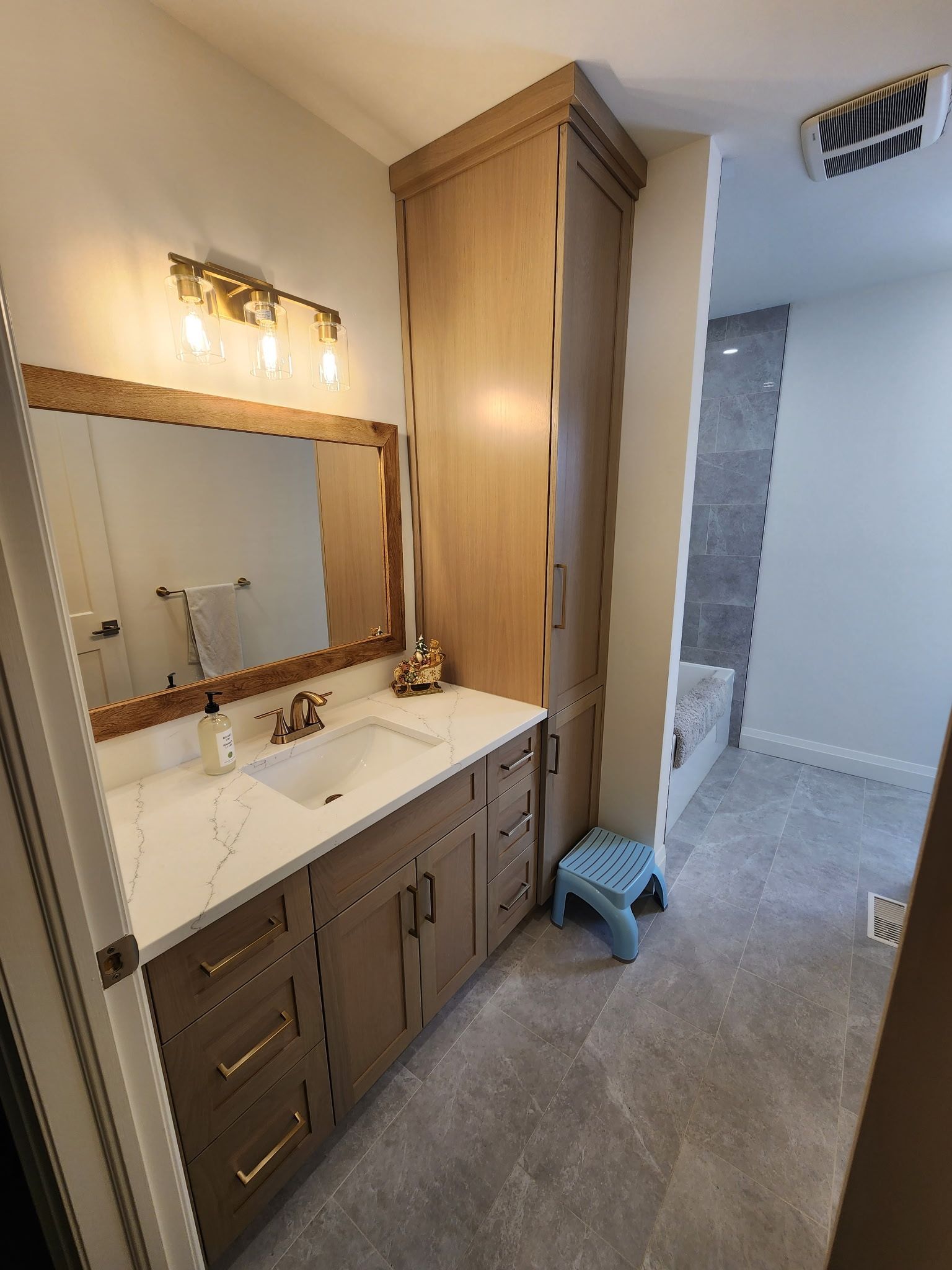 Bathroom with vanity, mirror, storage cabinet, and small blue step stool.