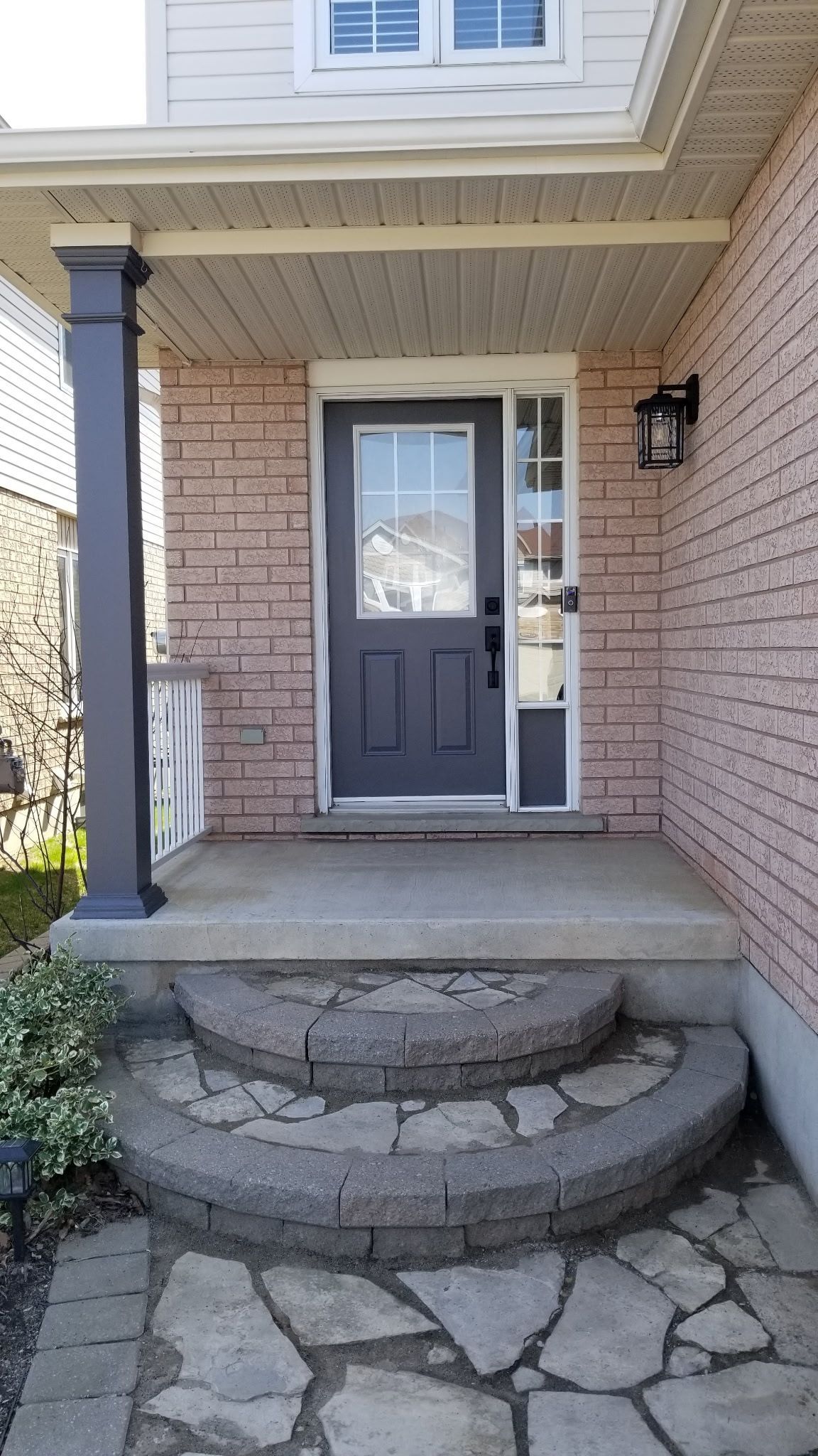 Front porch with steps leading to a gray door. Light brick exterior and a dark pillar.