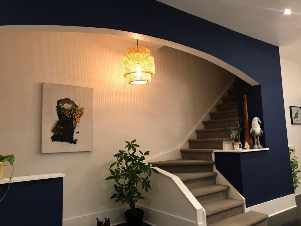 Entryway with white and navy blue walls, a staircase, artwork, and a hanging light fixture.