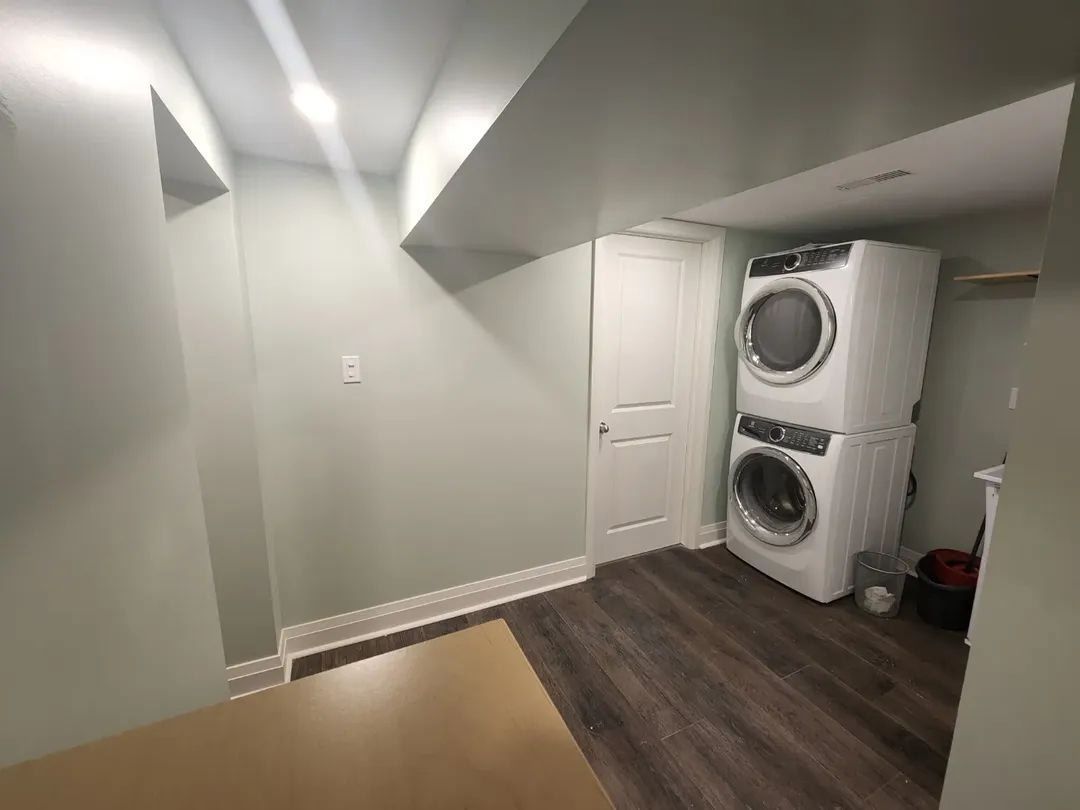 Laundry room with stacked washer and dryer, light green walls, wood-look flooring.