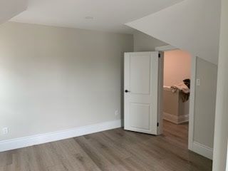 Empty room with white walls, a closed door, and wood flooring.