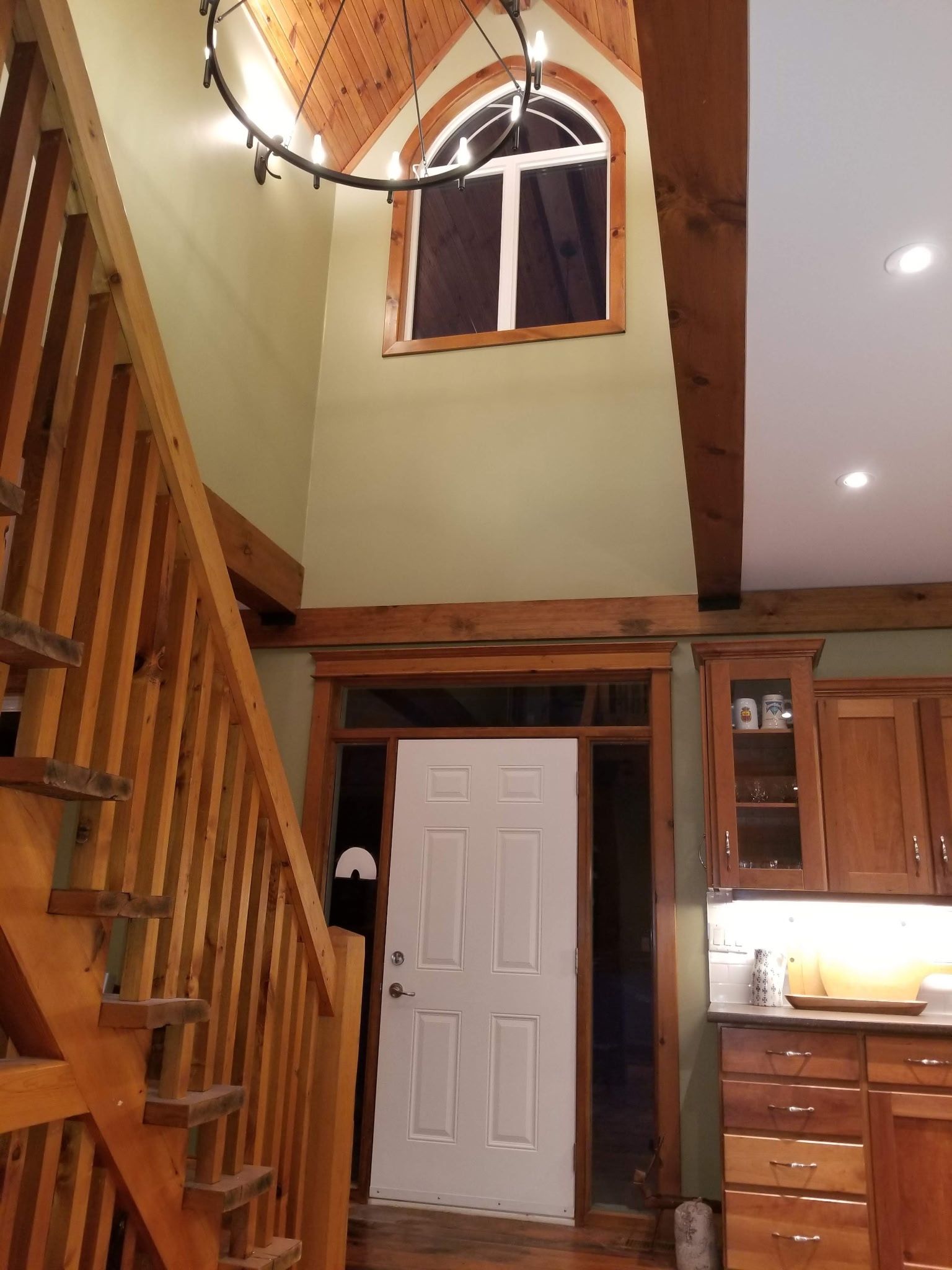 Interior view with wooden staircase, arched window, and door. Wooden beams, light green walls, and kitchen cabinetry.
