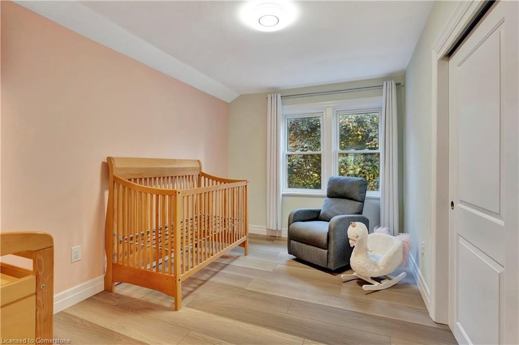 Nursery room with wooden crib, gray recliner, and white rocking swan. Light pink and beige walls, wooden floor.