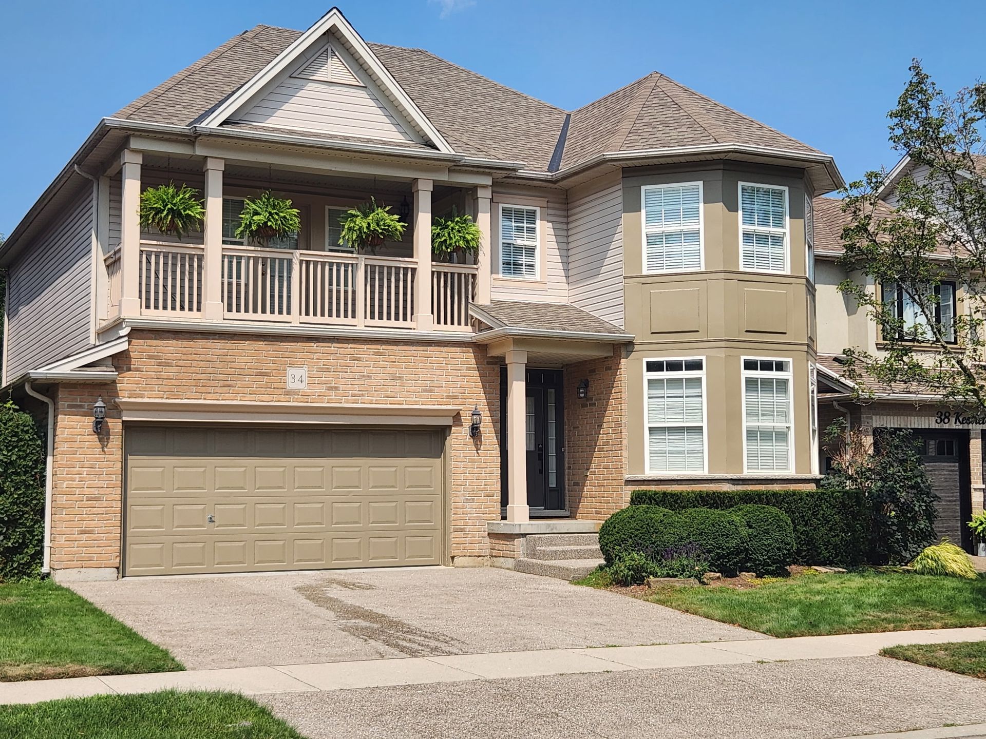 Two-story house with tan garage door, balcony, beige and tan exterior, and small front yard with green grass.