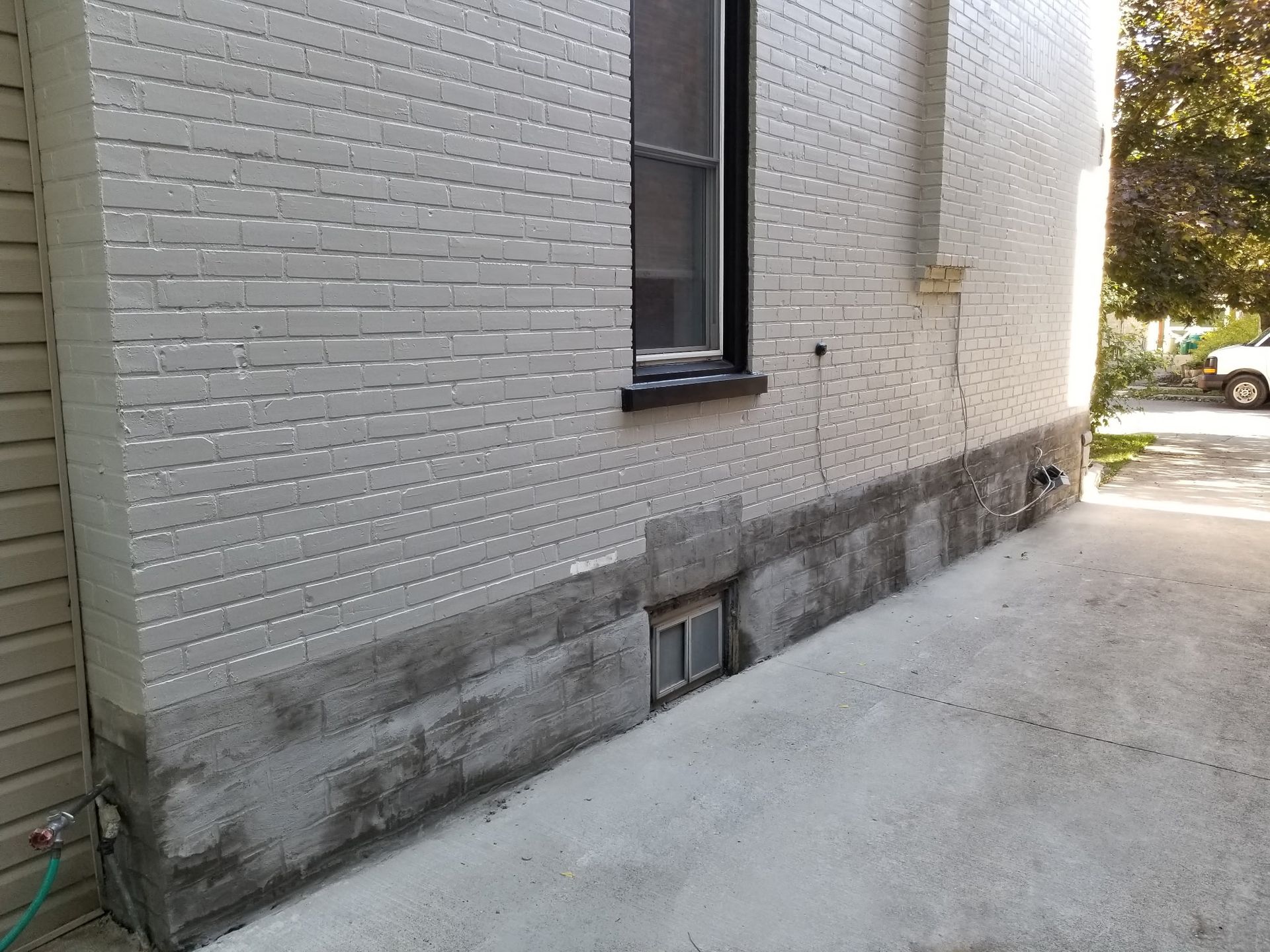 Exterior view of a building with a painted brick facade and a concrete foundation. A small window and a water spigot are visible.