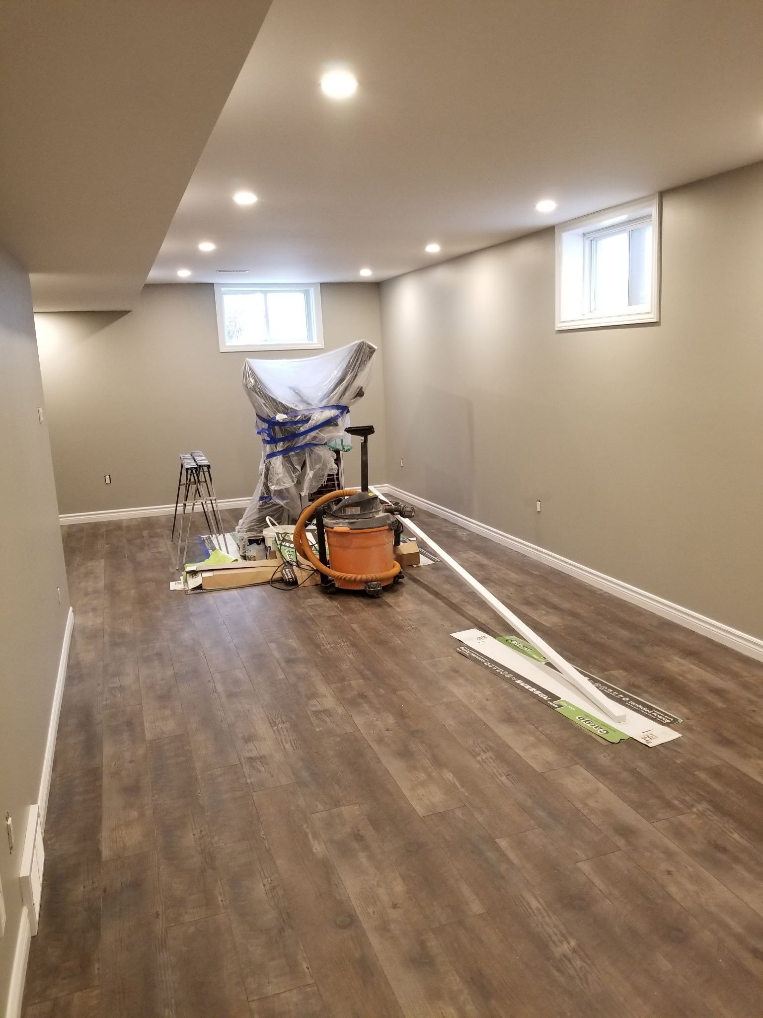 Basement interior with new wood flooring, neutral walls, recessed lighting, and construction equipment.