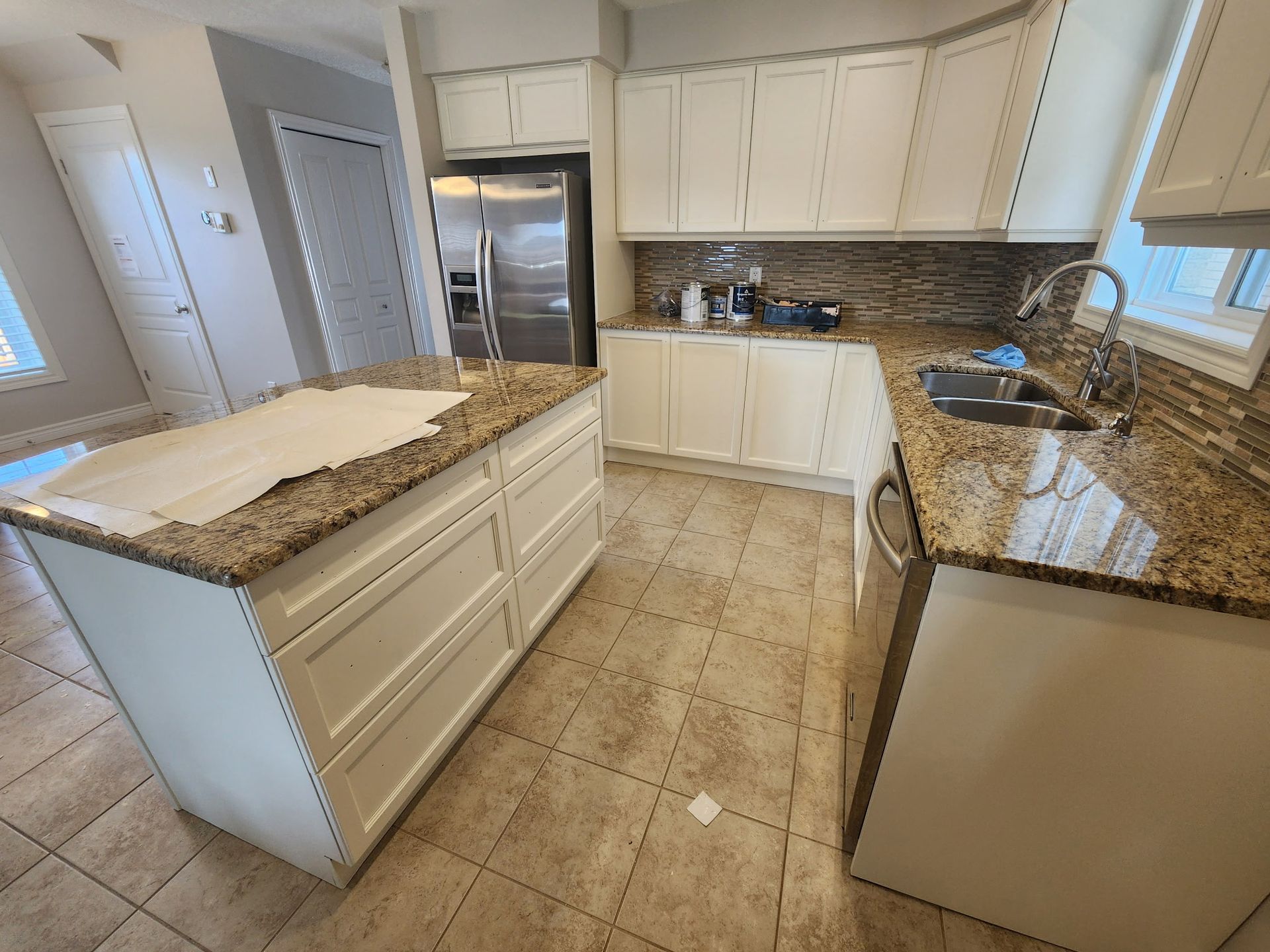 A kitchen with white cabinets, granite countertops, and a stainless steel refrigerator.