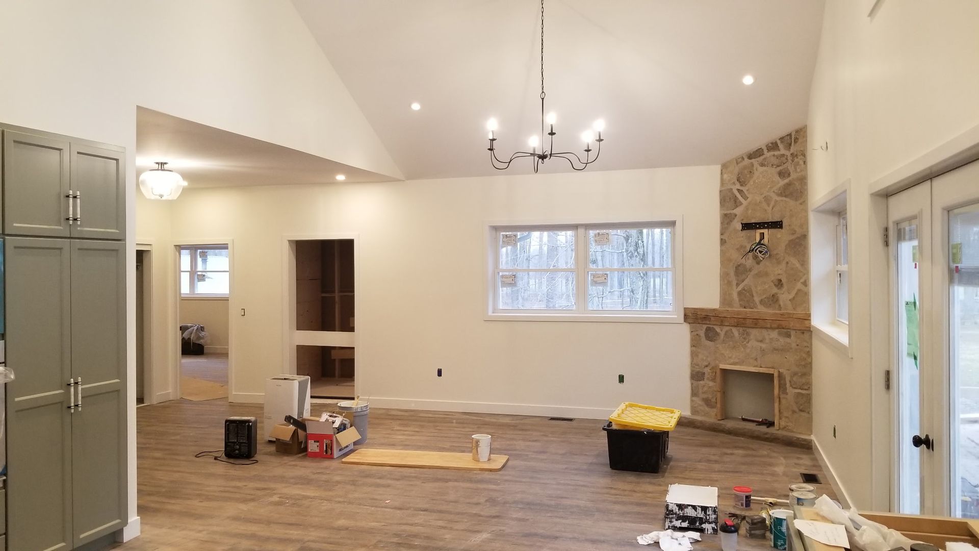 Interior view of a living space under renovation, with white walls, stone fireplace, and exposed wood floors.