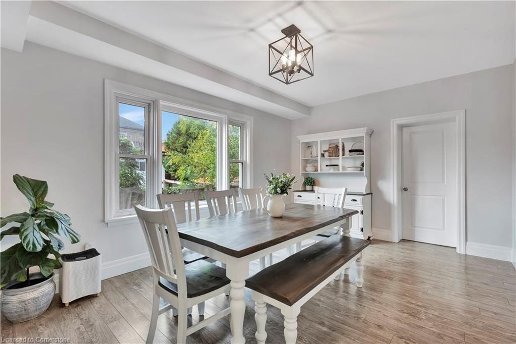 Dining room with white table, bench, chairs, and hutch. Large window and hardwood floors.