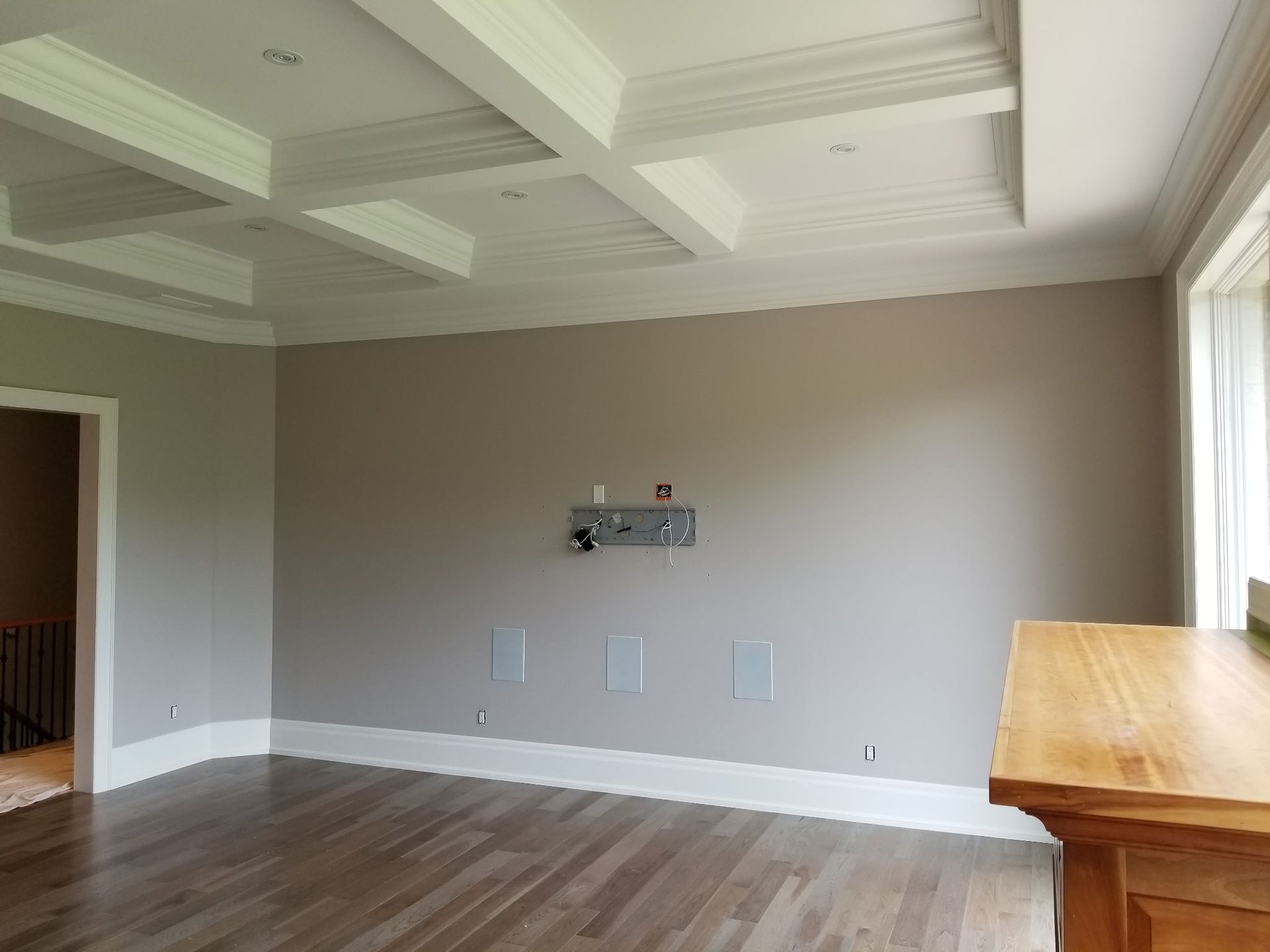 Empty room with beige walls, wood floor, white trim, recessed ceiling with coffers, and a small electrical box on the wall.