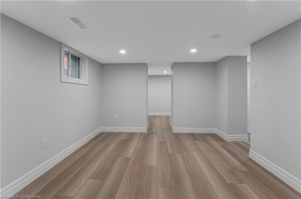 Empty, freshly painted room with wood-look flooring. Features a window, recessed lights, and doorway.