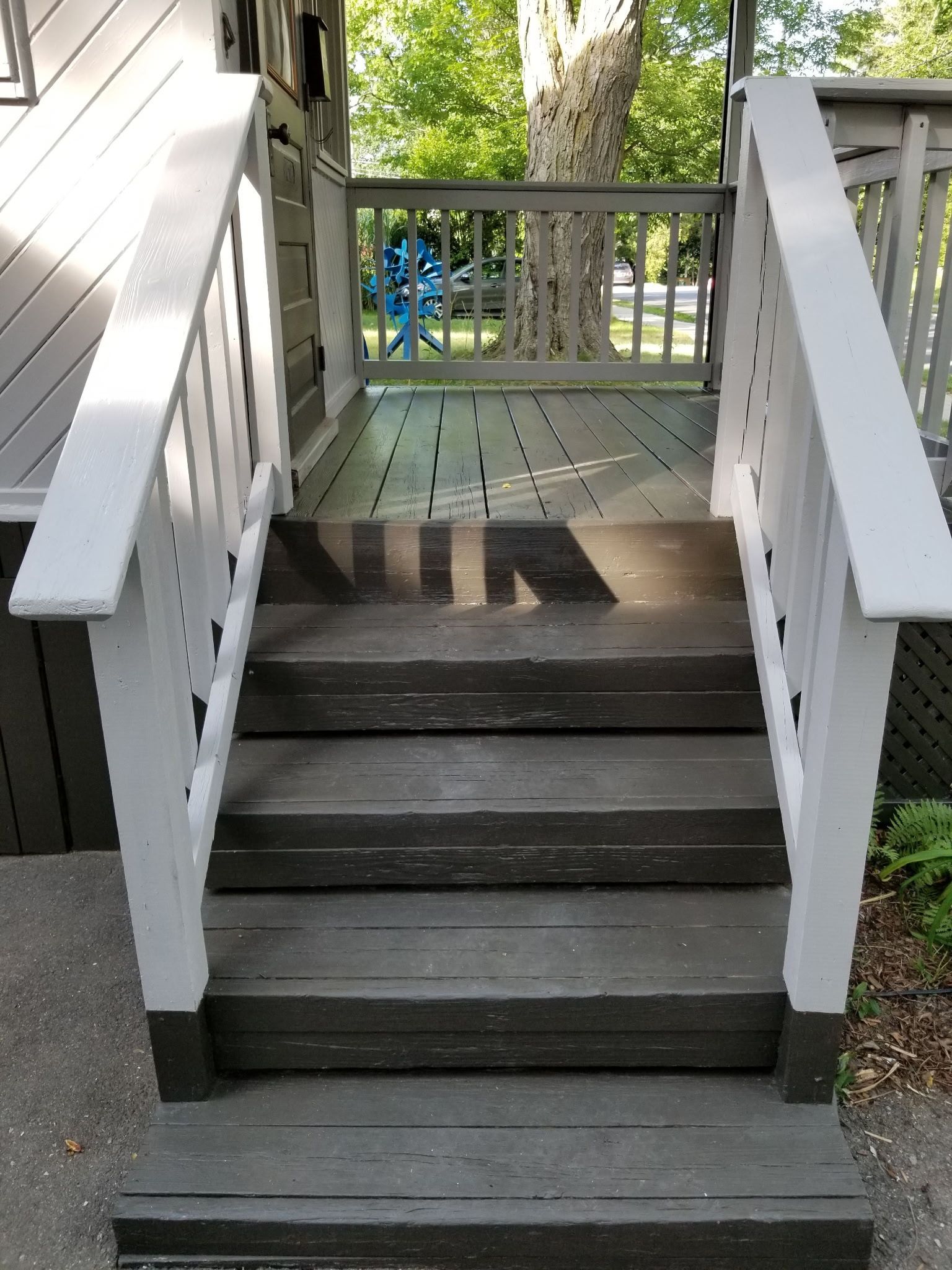 Wooden steps leading to a porch with white railings and a gray deck.