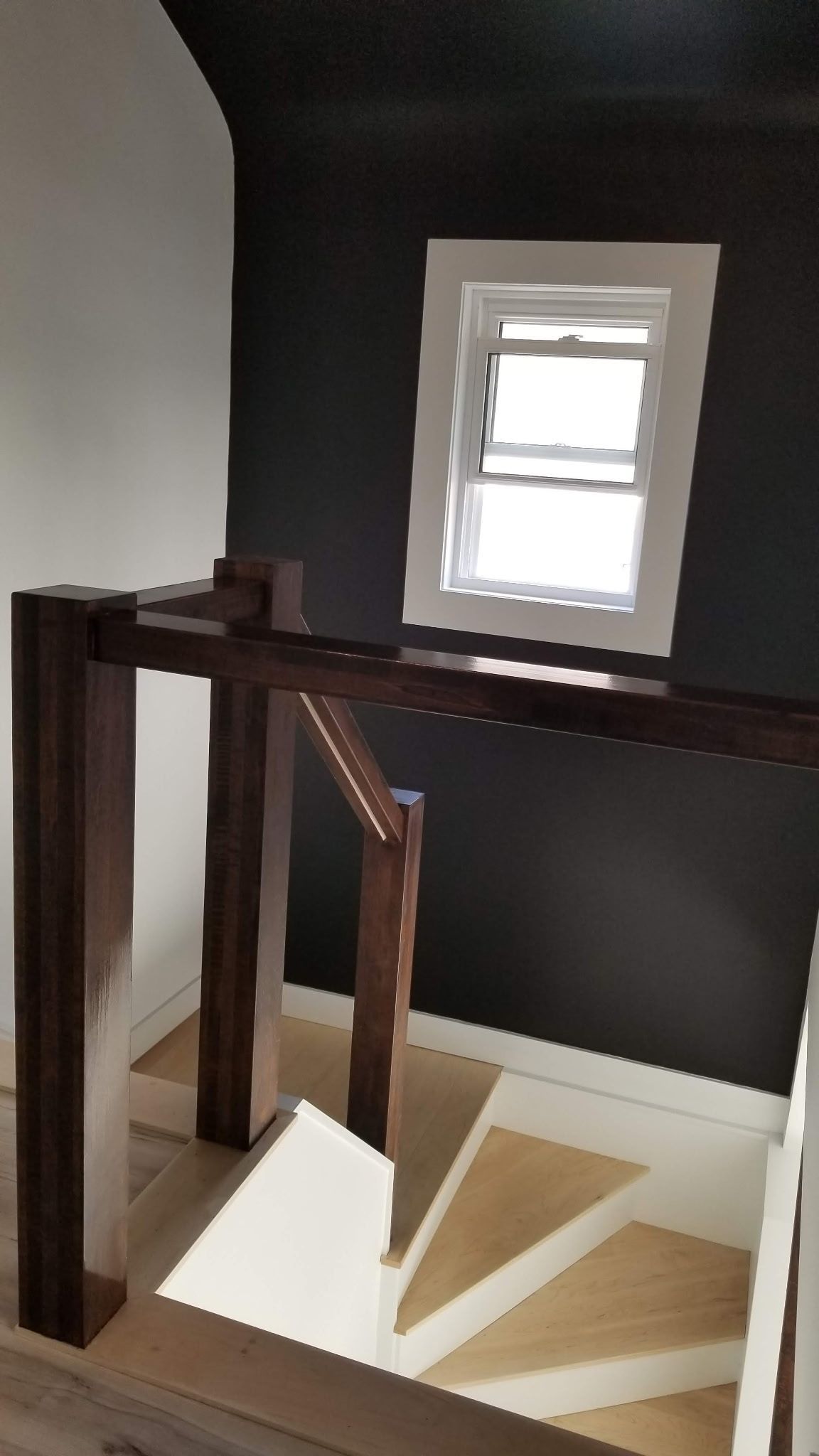 Staircase with dark stained wood handrail, white and tan steps, and a window on a dark wall.