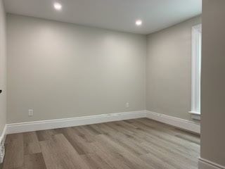 Empty room with light gray walls, white trim, and wood-look flooring. Two recessed lights are in the ceiling.