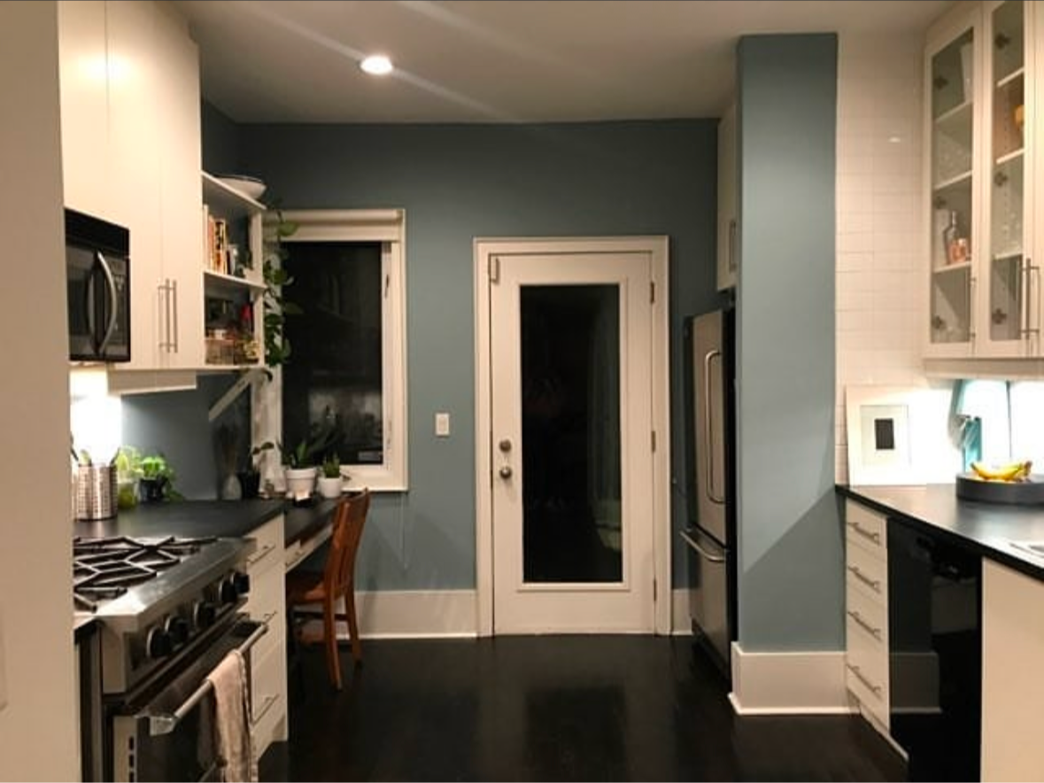 Kitchen with white cabinets, blue walls, dark floor, and a glass door.