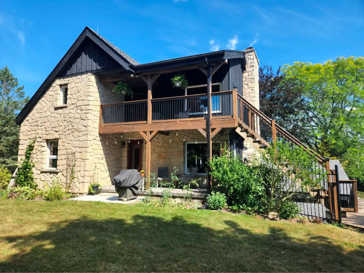 Stone house with wooden balcony, black roof, and green lawn on a sunny day.