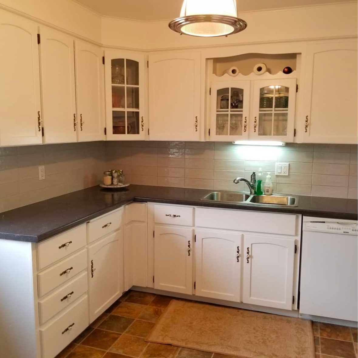 White kitchen cabinets with black countertops and tile backsplash.