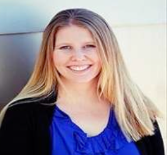 Woman with long blonde hair, smiling, wearing a blue shirt and black cardigan.