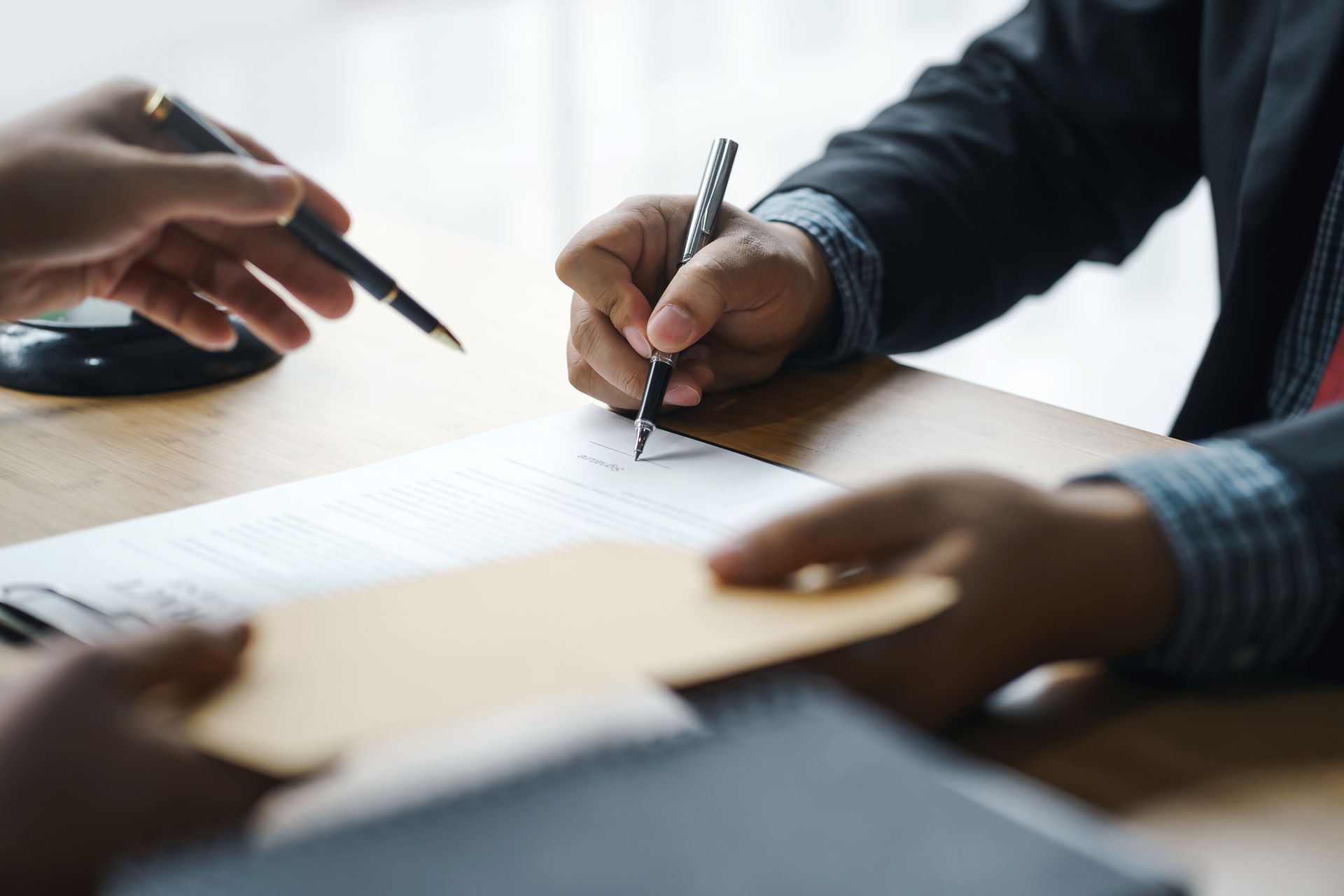 A man is writing on a piece of paper while another man holds an envelope.