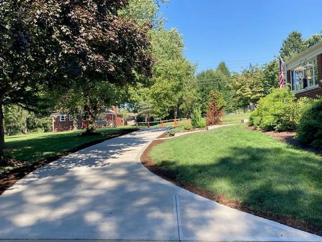 A concrete driveway leading to a house surrounded by trees and grass. - Gibsonia, PA - Langell Concrete Construction