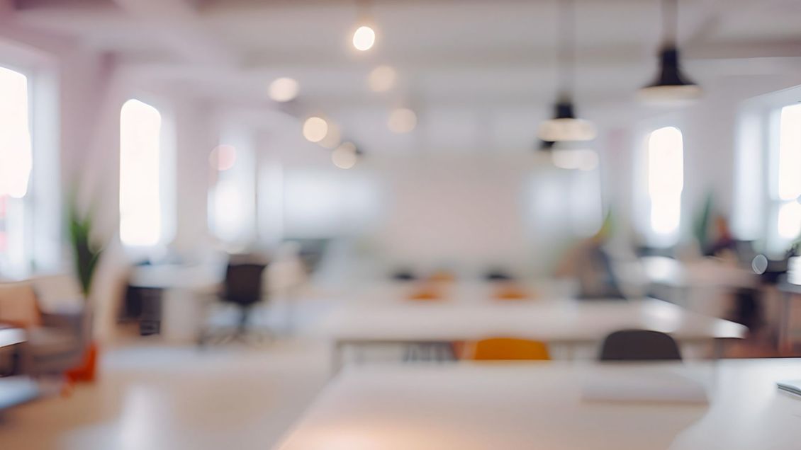 Blurred view of a bright, modern office with desks, chairs, and hanging lights.