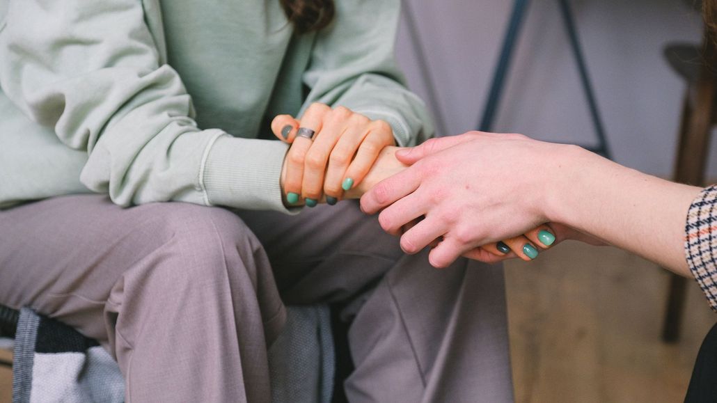 Person's hands clasped in support. One person wears a green sweater and the other a plaid shirt.