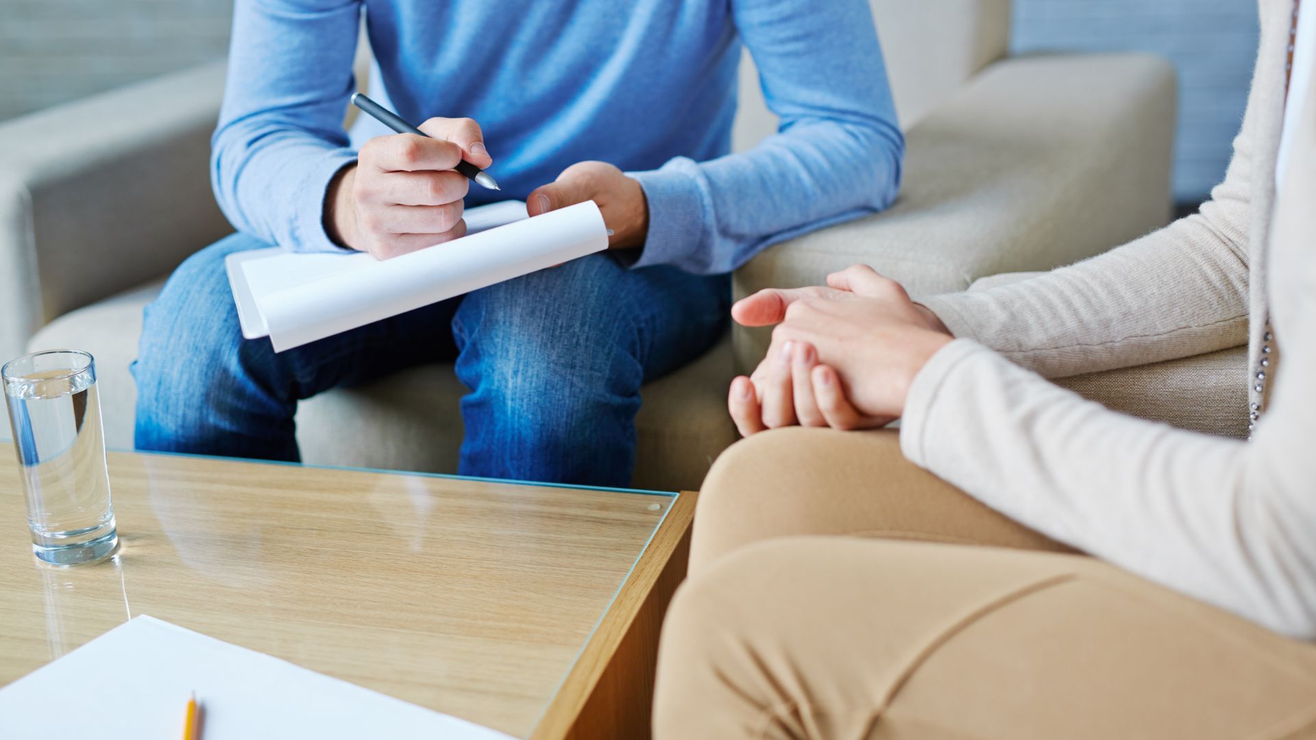 Therapist in green dress with clipboard, and patient gesturing hands on a sofa.