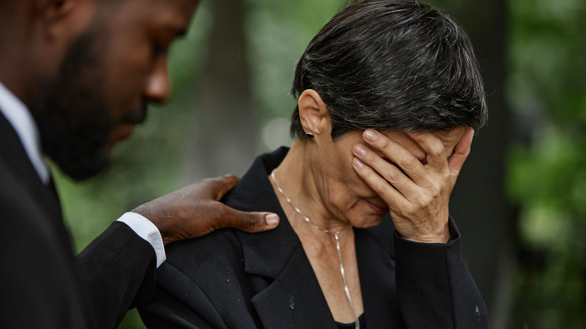 Person comforting someone grieving, hand on shoulder, woman covering face.