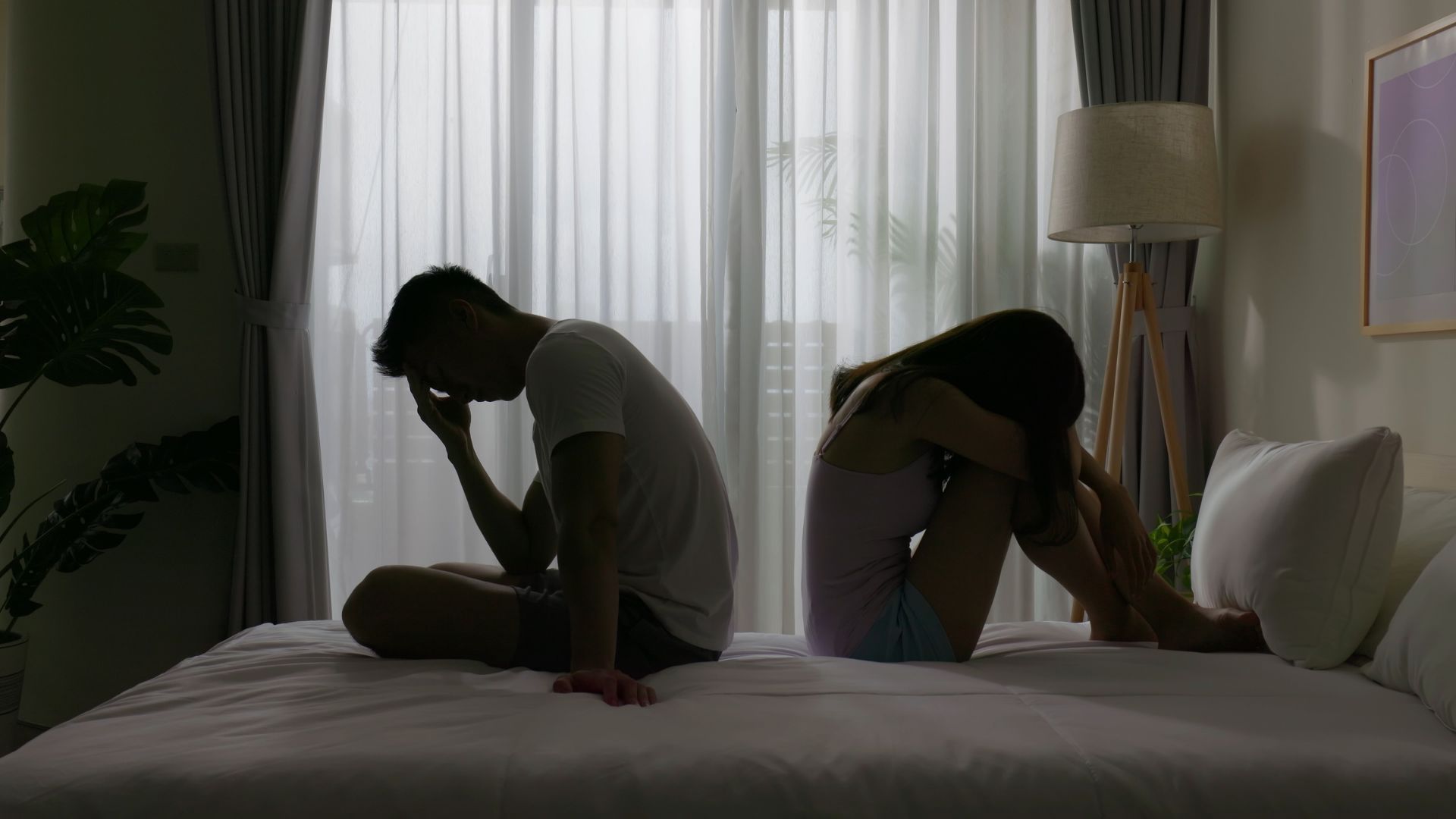 Woman awake and looking worried, beside sleeping man in bed.