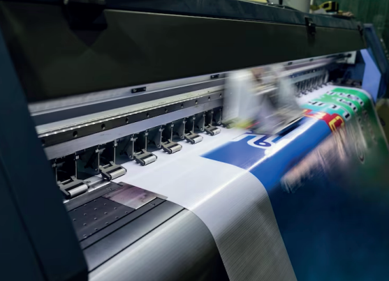 Impresora de gran formato en funcionamiento, imprimiendo una pancarta con gráficos azules, blancos y rojos.