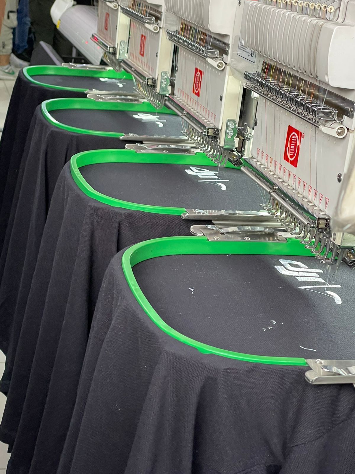 Máquinas de bordar cosiendo logotipos en camisetas negras, bastidores verdes, toma de primer plano.