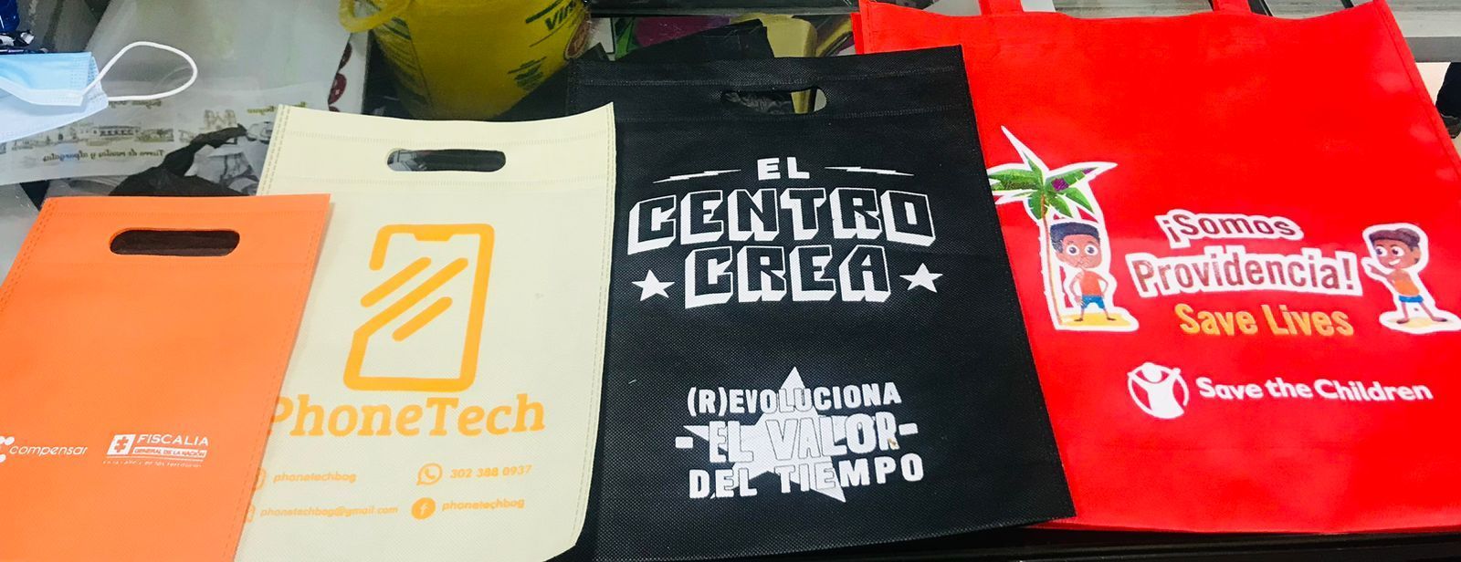 Se disponen cuatro bolsas de compra de distintos colores, cada una con logotipos impresos.