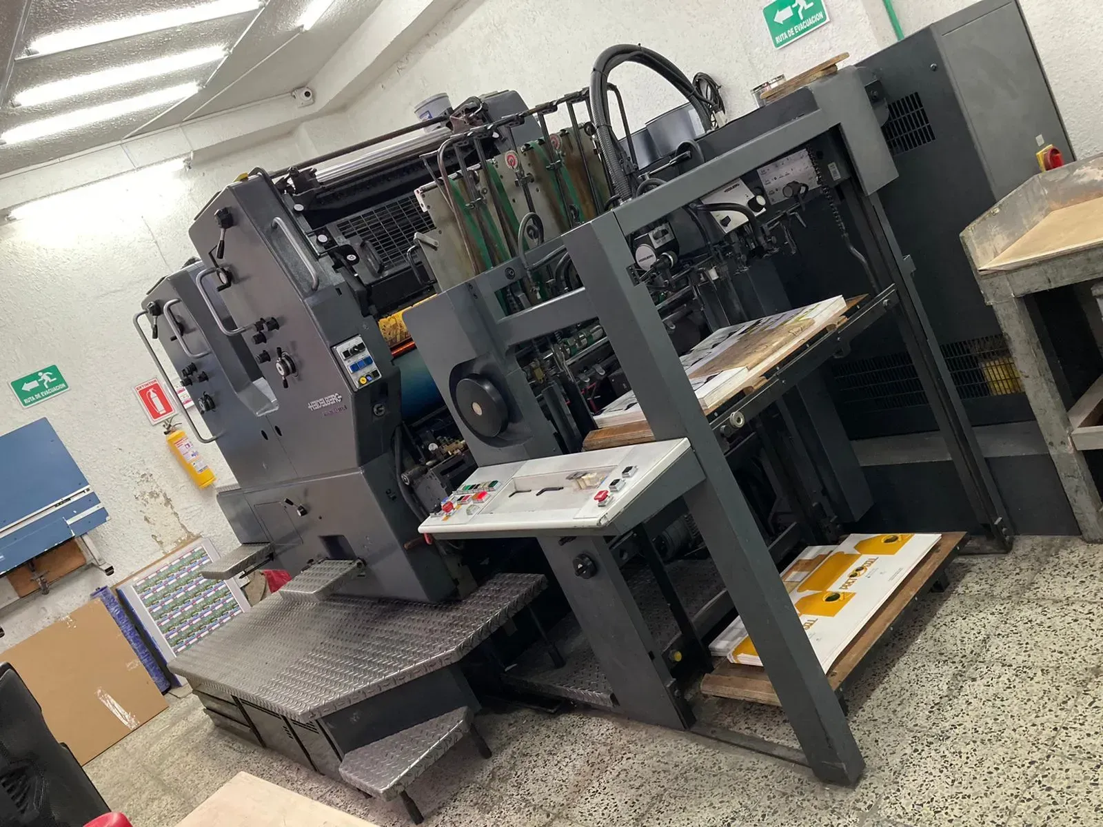 Prensa de impresión en una imprenta. Máquina gris oscura con panel de control, con pilas de hojas impresas visibles.