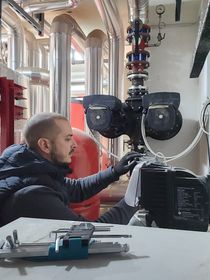 Un operaio ispeziona tubature e pompe industriali in una sala macchine.