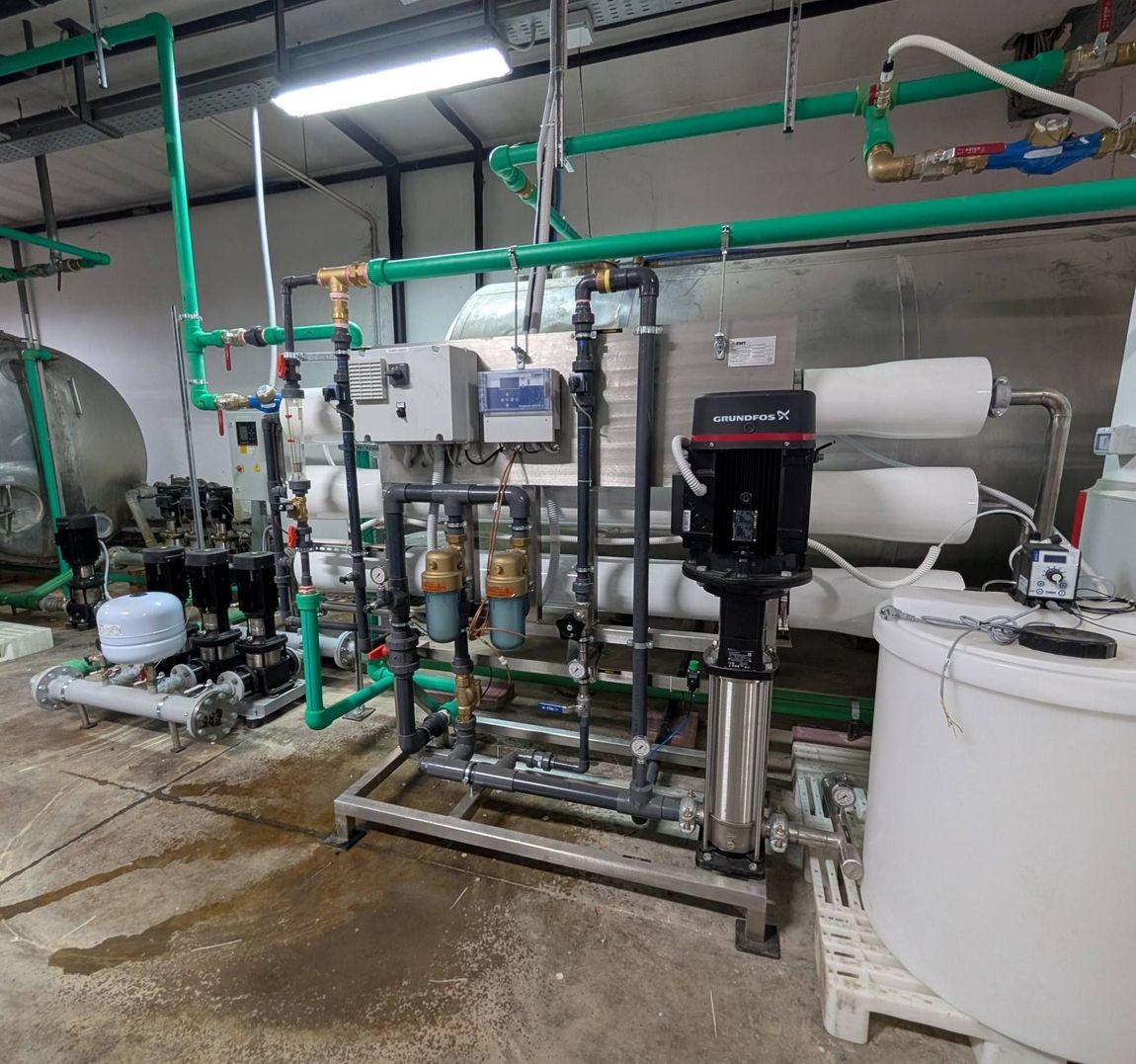 Sistema di filtrazione dell'acqua industriale con tubazioni, serbatoi e pompe di colore verde, installato in un locale tecnico.