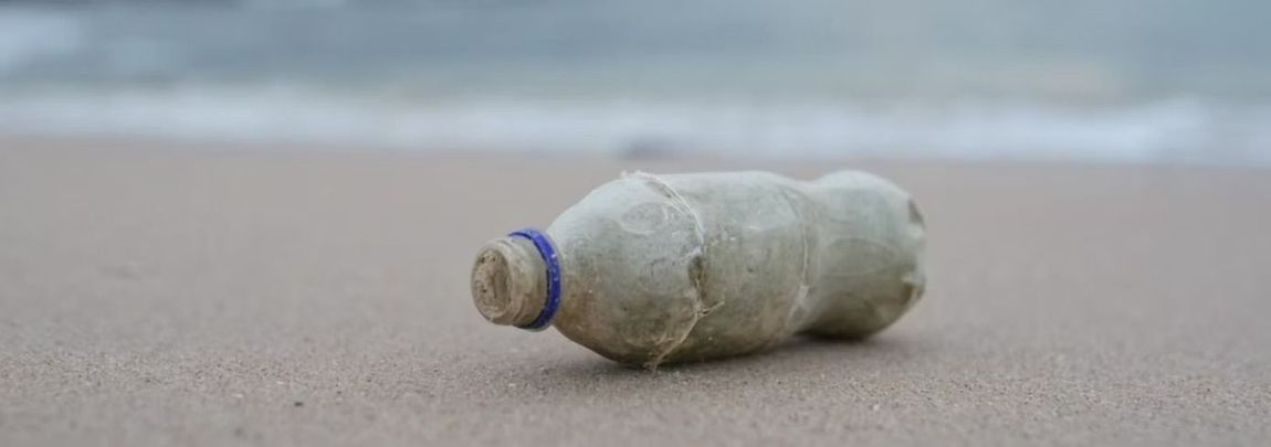 Bottiglia di plastica abbandonata su una spiaggia sabbiosa vicino alla battigia.
