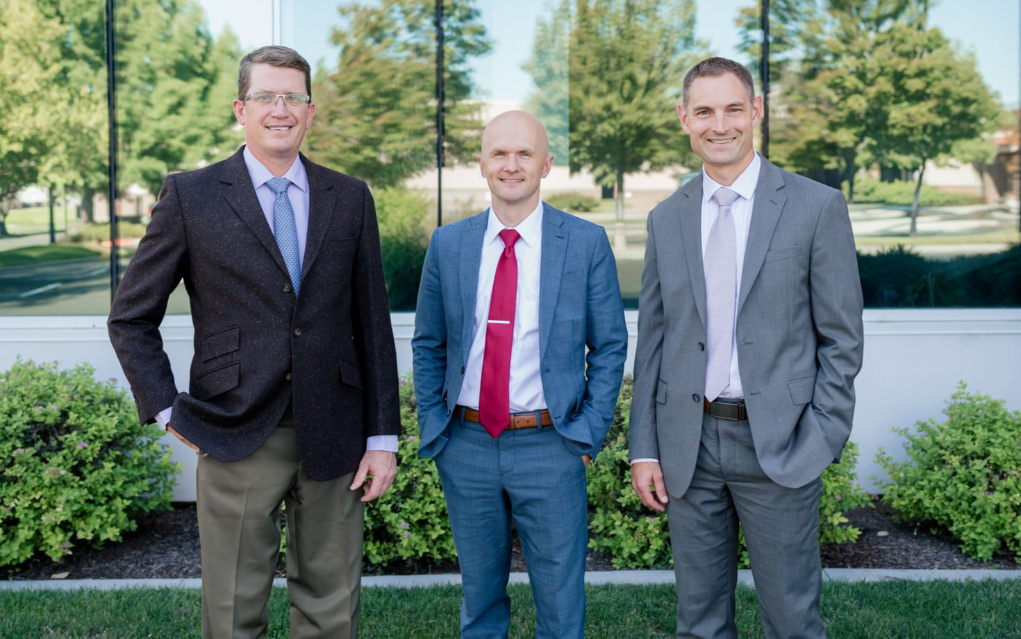 Four men in suits stand outside. They smile at the camera.