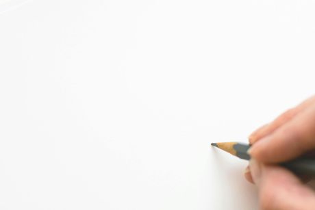 Hand holding a pencil, poised to draw on a blank white paper.