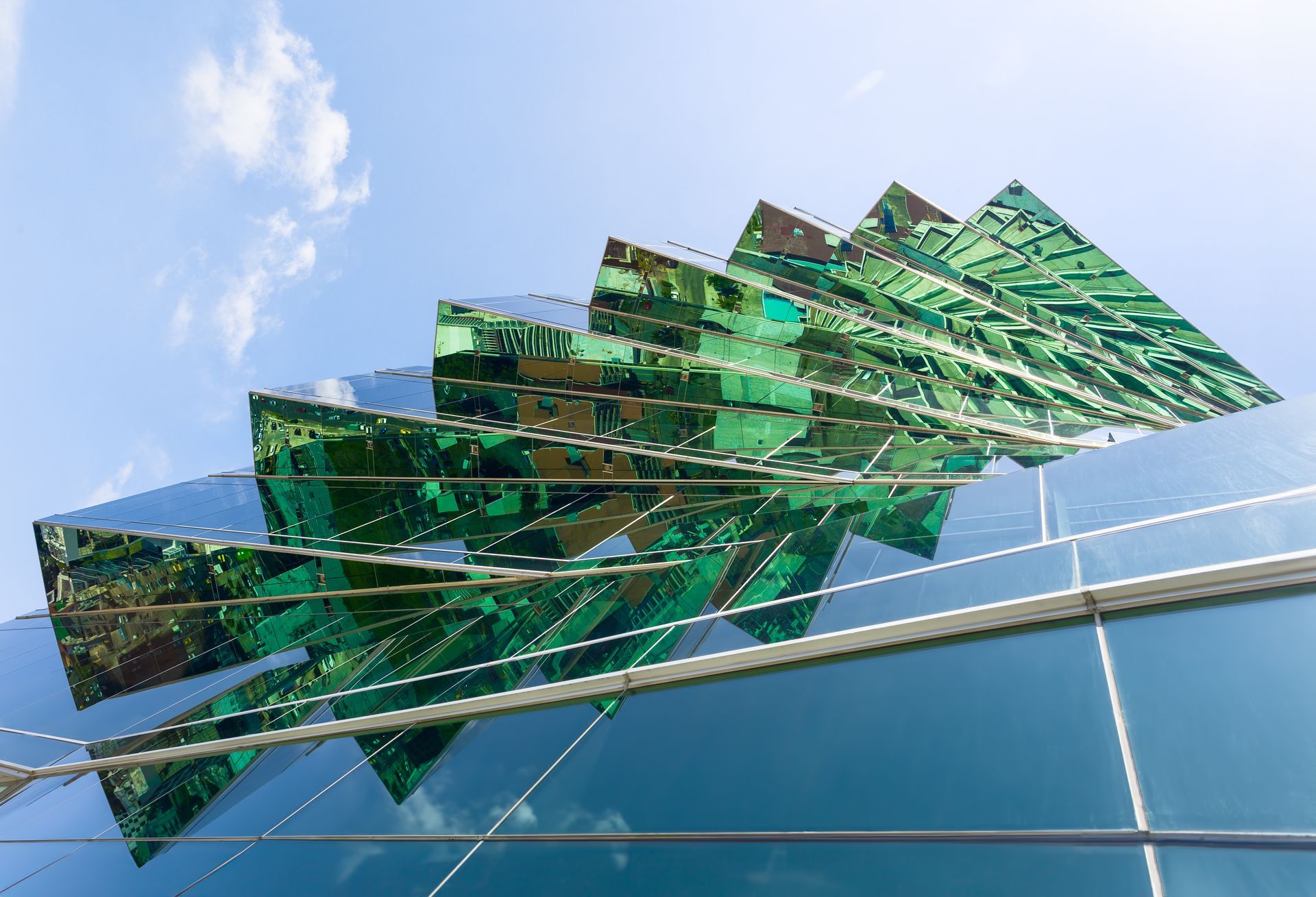 Una escultura verde en el costado de un edificio con un cielo azul de fondo.