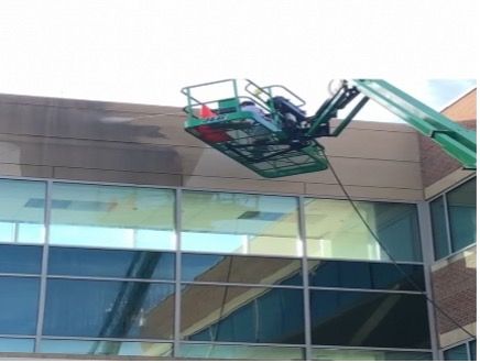A worker in a lift basket pressure washes a building's exterior.