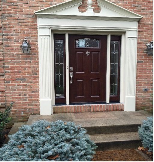 Dark wood front door with sidelights, brick exterior, and light trim.